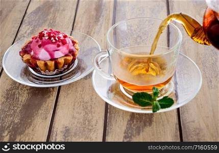 Cup of fresh strong tea with sugar and mint. Cup of tea with mint and teapot on a wooden background