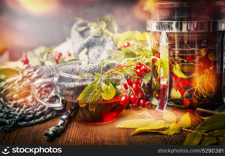 Cup of healthy tea with scarf, autumn leaves and berries on rustic wooden background. Hot autumn beverages concept