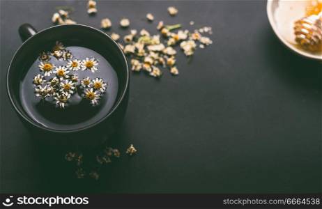 Cup of herbal chamomile tea with  dried chamomile flowers and honey on dark background, top view. Remedy to treat a wide range of health issues. Herbal medicine concept. Healing herbs.