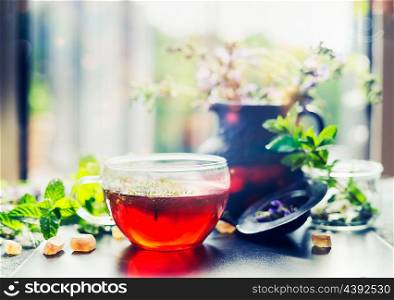 Cup of herbal tea with fresh herbs and sweets on window still