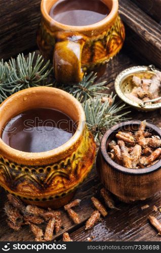 Cup of herbal tea with pine buds on wooden background.Mug of herbal tea on aged rustic background. Tea with pine buds