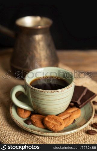 Cup of hot black coffee, cookies and chocolate on a brown wooden background