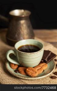 Cup of hot black coffee, cookies and chocolate on a brown wooden background