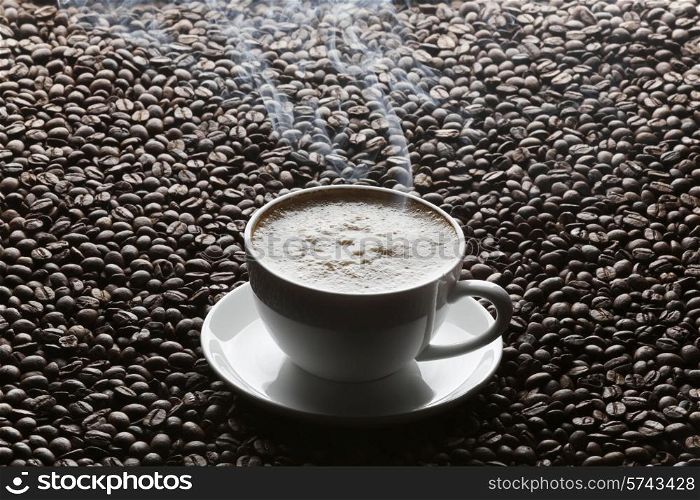 Cup of hot cappuccino on roasted coffee beans