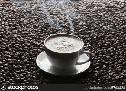 Cup of hot cappuccino on roasted coffee beans