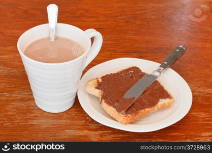 cup of hot chocolate and sweet sandwich from fresh toast with chocolate spread, table knife on wooden table