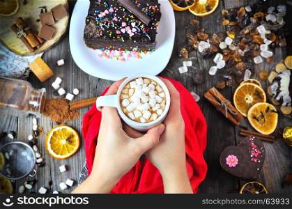 Cup of hot chocolate with white marshmallow in female hands over the table, top view
