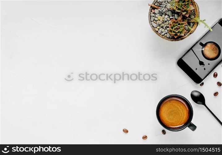 Cup of hot espresso with foam, located on a wide white background with copy space. Flat lay, restreto in a black cup, a smartphone and a garok with a flower on the background