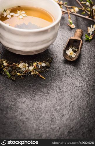 Cup of Jasmine tea with fresh flowers on dark background, copy space
