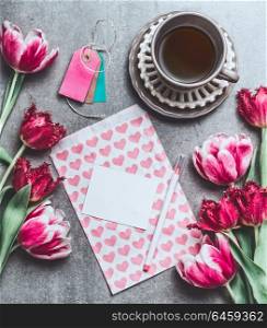 Cup of morning coffee with tulips flowers and blank paper card mock up with hearts, top view. Holidays breakfast. Flat lay style. Greeting card concept