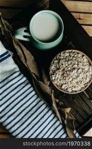 Cup of oat milk with oat seed on a bowl over a wooden plank