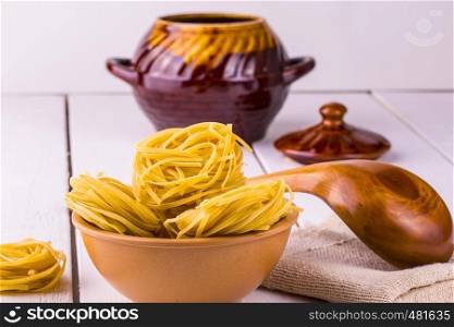 cup of spaghetti and a wooden spoon on a background of a clay vessel on a wooden white table