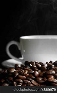 Cup of steaming coffee on coffee beans on black background