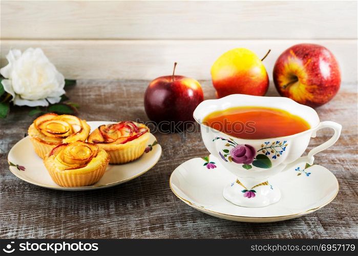 Cup of tea and apple rose shaped muffins. Homemade apple cake for tea time. Breakfast tea with sweet apple pastry. . Cup of tea and apple rose shaped muffins