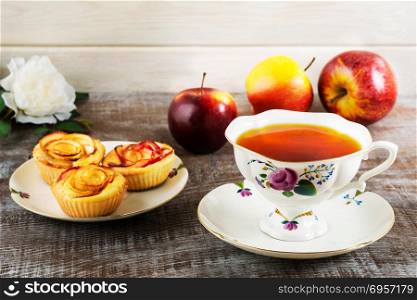 Cup of tea and apple rose shaped muffins. Homemade apple cake for tea time. Breakfast tea with sweet apple pastry. . Cup of tea and apple rose shaped muffins