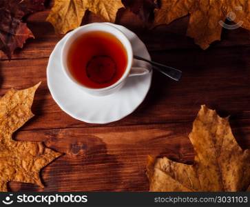Cup of tea and maple leaves in the background on a wooden.Dark style photo. Tea and maple leaves on a wooden background