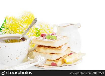 Cup of tea and pile of waffles with raspberries isolated on a white background