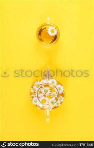 Cup of tea and transparent teapot with camomile flowers on yellow background. Chamomile Tea Benefits Your Health concept. Top view.. Cup of tea and transparent teapot with camomile flowers on yellow background. Chamomile Tea Benefits Your Health concept. Top view