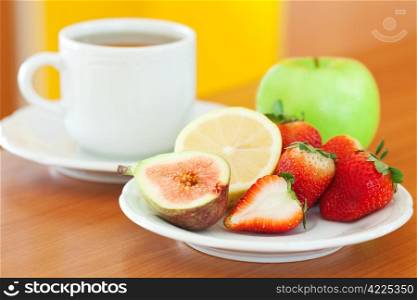 cup of tea, apple, lemon, fig and strawberries on a plate