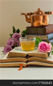 Cup of tea in glass cup with brass teapot, old books and rose flowers. Cup of tea with books