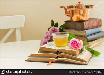 Cup of tea in glass cup  with teapot, old books and rose flowers. Cup of tea with books