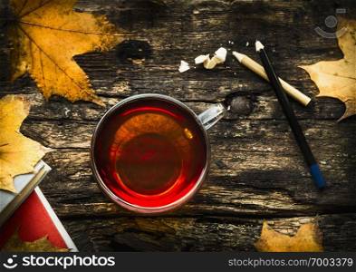 cup of tea with autumn leaves, books and pencils on wooden background, top view