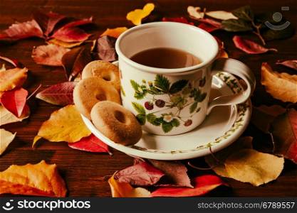 Cup of tea with biscuits and autumnal foliage over a dark table. Cup of tea with biscuits and autumnal foliage