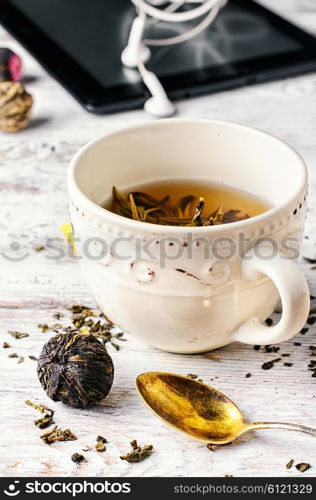 Cup of tea with infused rose and defocused portable computer. Morning tea and tablet