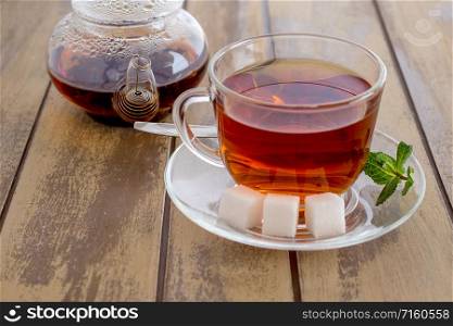 Cup of tea with mint and teapot on a wooden background. Cup of fresh strong tea with sugar and mint