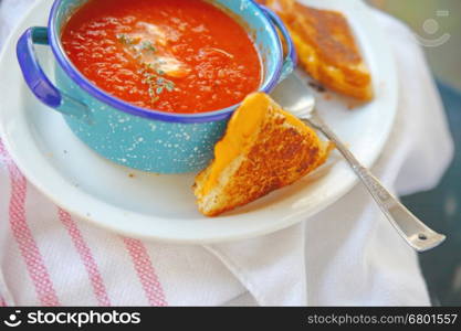 Cup of tomato soup with fresh thyme and grilled cheese sandwich