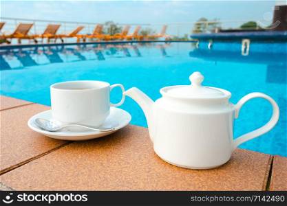 cup on the table near the pool . White ceramic coffee cup
