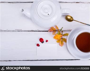 cup with black tea and white paper business card on a wooden background, top view