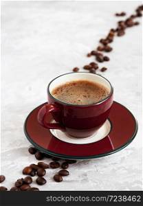 Cup with burgundy espresso located on a saucer, on a gray background. Roasted coffee beans are located around a cup of coffee.