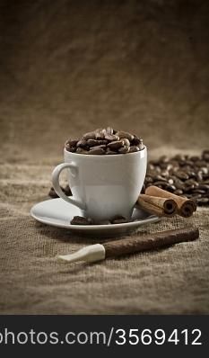 cup with coffee beans and cinnamon on burlap