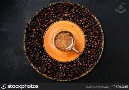 Cup with coffee espresso arranged on a dark background. Roasted coffee beans are located around a cup of coffee.Top view