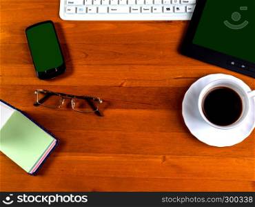 cup with coffee, office supplies and gadgets with a green screen. View from above. Table space with a cup of coffee, eyes and electronic gadgets