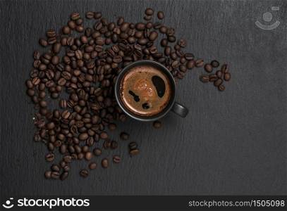 Cup with espresso, around a cup of coffee beans, a black stone background, copy space for text. Top view. Coffee time