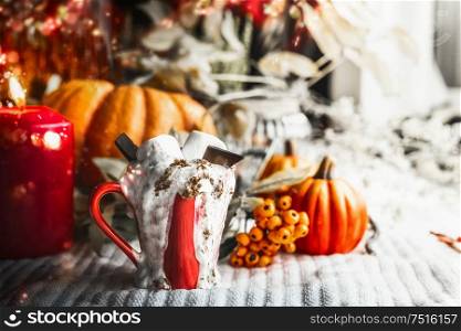 Cup with hot chocolate and marshmallow at window with candle and pumpkins. Autumn mood. Cozy home still life