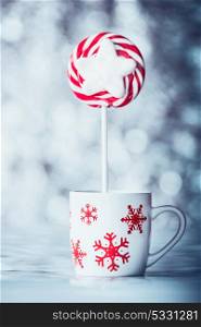 Cup with snowflakes and Christmas candy on blue bokeh background, front view