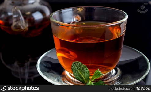 Cup with tea and a leaf of mint on black glass. Cup of tea with a leaf of mint on a black background