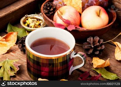 Cup with tea on an autumn background of fallen leaves, apples and grapes.Autumn still life. Cup of tea with autumn leaves