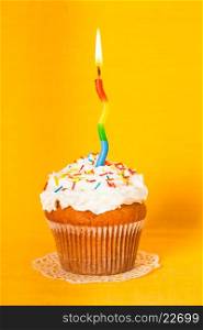 Cupcake with one burning candle on yellow napkin. Cupcake with candle