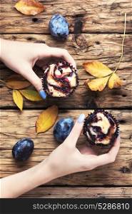cupcake with plum. Hand with cupcake above the table with autumn leaves