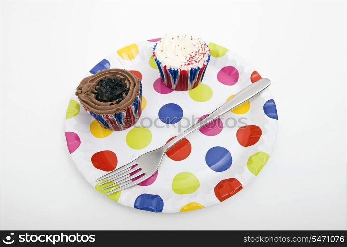 Cupcakes and fork in multicolored plate against white background