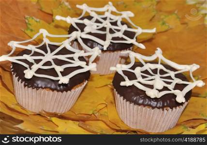 Cupcakes with chocolate glaze with a network of white chocolate on a background of autumn leaves