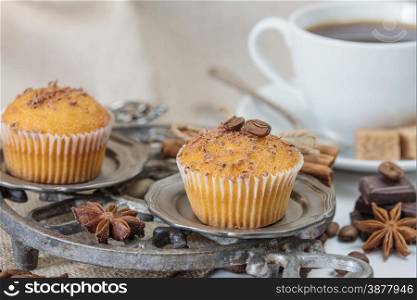 Cupcakes with chocolate shavings and white coffee cup surrounded by coffee beans and a variety of spices with space for text