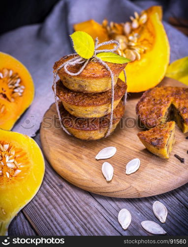 cupcakes with pumpkin on a round wooden board, next to pieces of fresh pumpkin