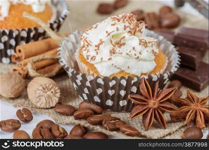 Cupcakes with whipped cream and chocolate shavings surrounded by coffee beans and a variety of spices