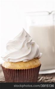 Cupcakes with white cream on background of a carafe of milk on wooden table. Cupcakes with white cream on background of a carafe of milk