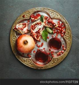 Cups of Pomegranate tea and fresh pomegranates on dark background, flat lay